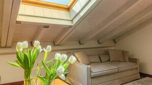A cozy attic bedroom with a skylight, a beige sofa, and a vase of white tulips. - Casa Pegaso in Canton de Fiori (Bologna)