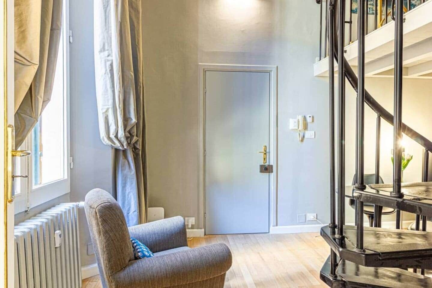Un soggiorno moderno con un divano grigio, un termosifone, una porta e una scala.