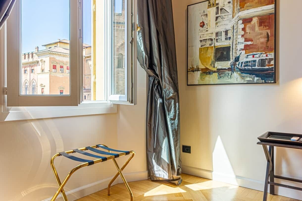 Ein Zimmer mit Fenster, einem Bild, einem Klappstuhl und einem kleinen Tisch.