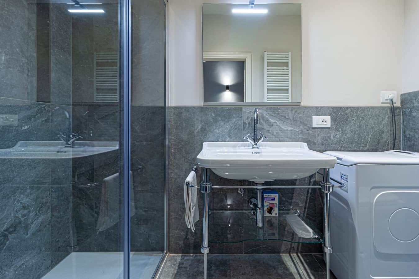 A modern bathroom with a glass shower enclosure, a white sink, and a built-in washing machine.