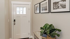 Een hal met een witte deur, een kamerbreed tapijt met patroon, een console tafel met een plant en lijstjes met foto’s aan de muur.