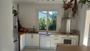 Cozinha moderna com armários brancos, lava-louças embutida, pia de aço inoxidável e janela com vista para o verde lá fora.
