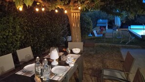 Uma área de refeições ao ar livre com uma mesa posta para dois, cercada por vegetação e luzes de Natal.