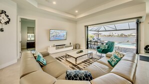 Un salon moderne avec un ensemble de canapés, une table basse, un téléviseur et une vue sur l’eau.