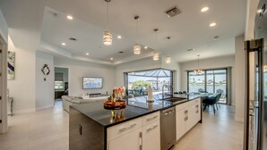 Une cuisine moderne dotée d’un grand îlot central, de luminaires suspendus et offrant une vue sur l’extérieur.