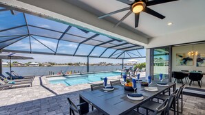 Un espace extérieur abrité comprenant une piscine, une table à manger et des chaises, avec vue sur une étendue d’eau.