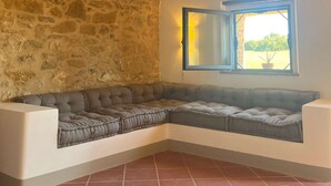 A corner room with a stone wall, a cushioned bench, a window with a view, and a tiled floor. - Podere Sole - “Alba” - Private apartment in a farmhouse with vineyards and nature in Tuscany (Trequanda)