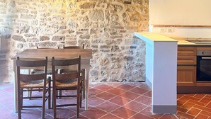 A rustic kitchen with exposed stone walls, wooden beams, a tiled floor, and basic cabinetry. - Podere Sole - “Alba” - Private apartment in a farmhouse with vineyards and nature in Tuscany (Trequanda)