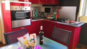 A compact kitchen with red cabinets, a built-in oven, a gas stove, and a dining table with chairs. - Celeste sea view vacation home with parking (Portici)