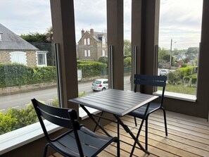 Ein Balkon mit Tisch und zwei Stühlen, mit Blick auf eine Straße mit Häusern und parkenden Autos.