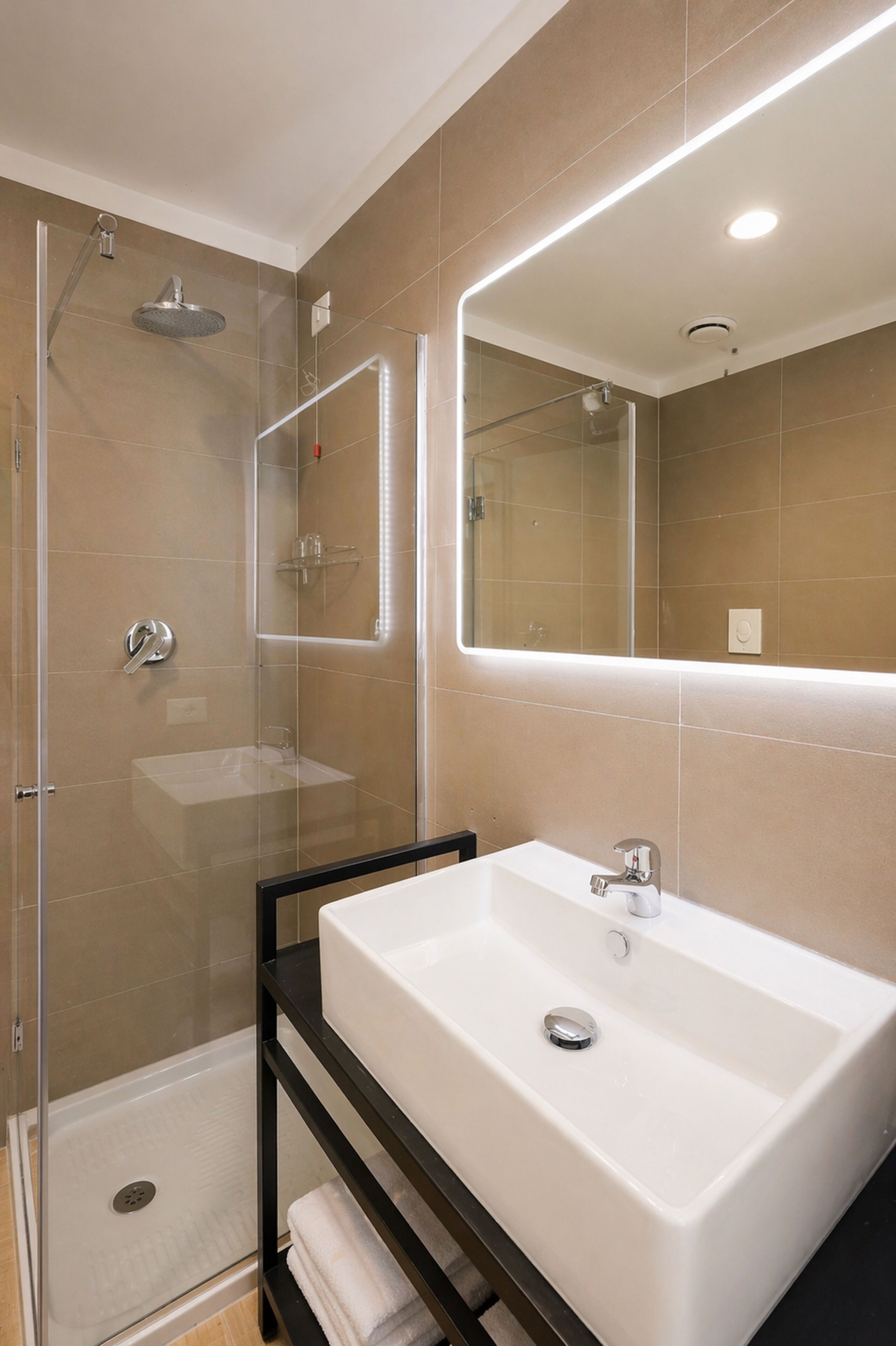 A modern bathroom with a glass-enclosed shower, a white sink, and a large mirror.