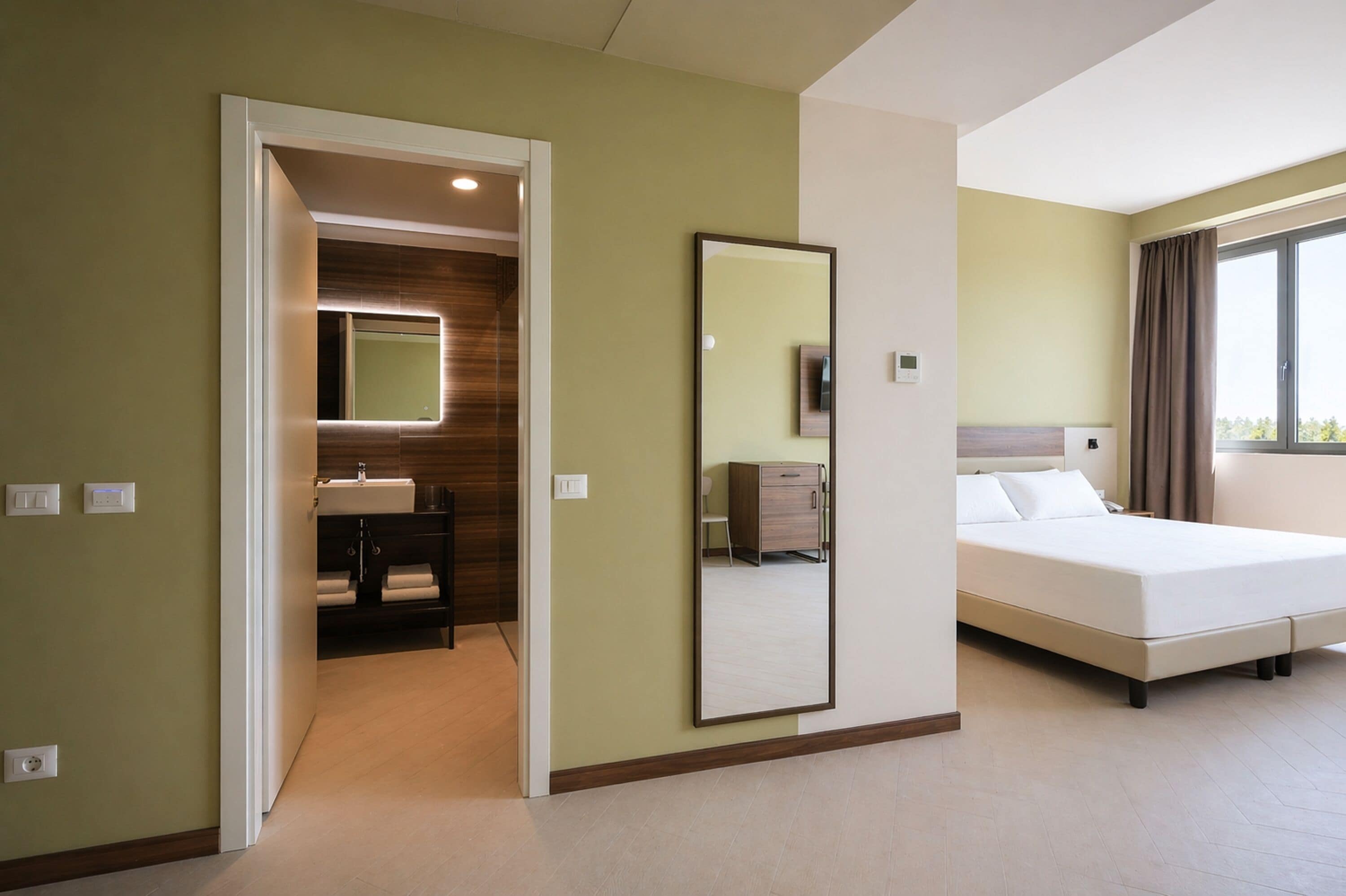 A hotel room with a bed, a bathroom with a mirror, and a view of the outdoors.