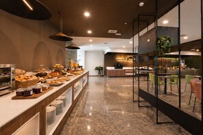 Ein modernes Frühstücksbuffet mit verschiedenen Speisen, einer Kaffeestation und einem Sitzbereich mit Stühlen.