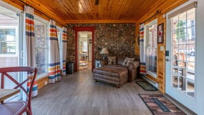 A log cabin interior with a stone wall, wooden ceiling, and a cozy seating area with a sofa and ottoman. - The Blackbird Inn on Rice Lake (Rice Lake)
