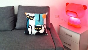 En moderne stue med en grå sofa, en pyntepude, et sengebord med skuffe, og en væg med et 'WOW' skilt.
