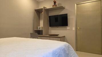 Quarto com cama, escrivaninha, cadeira, televisão e guarda-roupa.