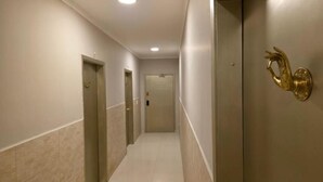 Egy folyosó, melynek mindkét oldalán ajtók találhatók, a mennyezeten egy lámpatest, a falon pedig egy díszes, sárgaréz tárgy.