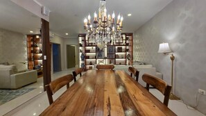Un comedor con una mesa de madera, sillas, una araña y estantes con objetos decorativos.