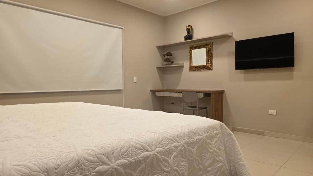 Un dormitorio con una cama grande, un escritorio con silla, un televisor y una estantería con adornos.