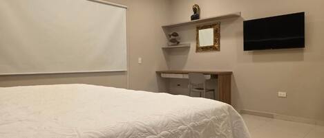 Un dormitorio con una cama grande, un escritorio con silla, un televisor y una estantería con adornos.