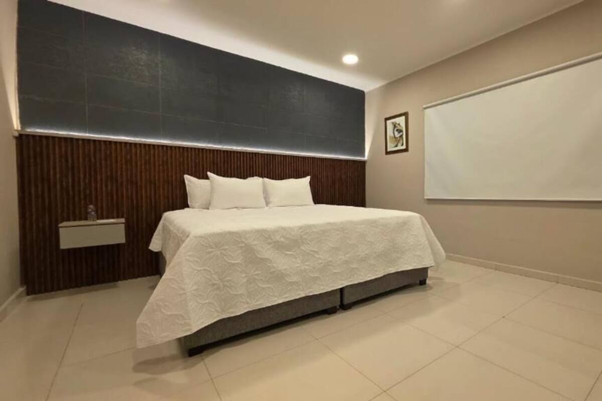 Een moderne slaapkamer met een groot bed, een nachtkastje, een aan de muur bevestigde televisie en een houten hoofdbord.