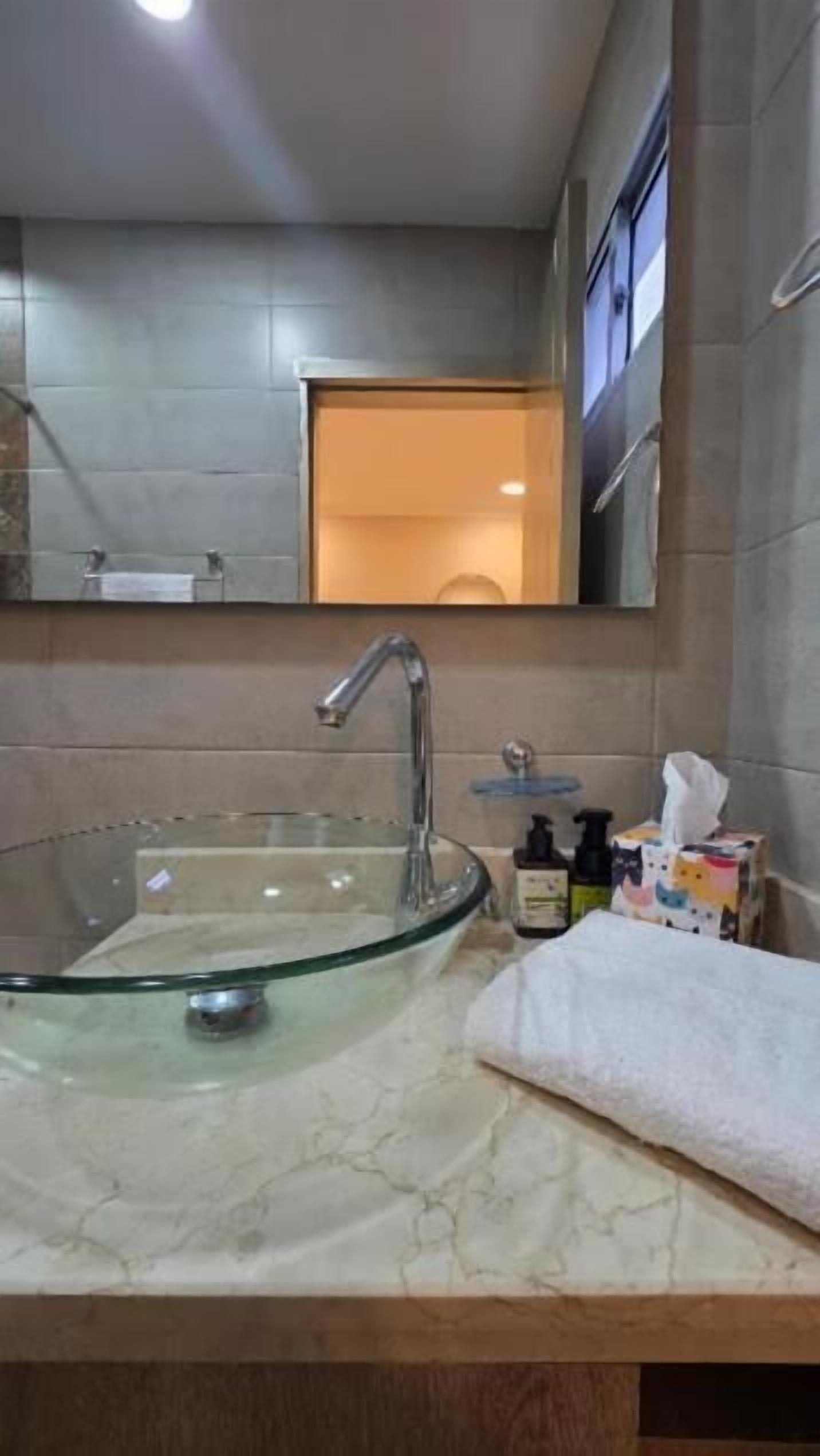 Un baño con un lavabo de vidrio, un espejo y una toalla.
