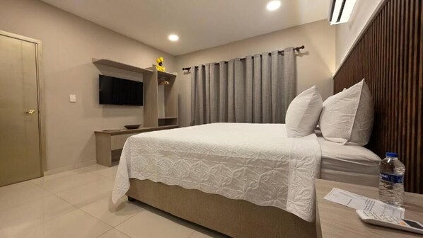 A bedroom with a bed, a TV mounted on the wall, a wooden headboard, and a curtain. - HOTEL CASA LA TABLADA AEROPUERTO (Cartagena)