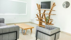 A modern living room with a grey sofa, a wooden coffee table, and a TV mounted on a wooden shelf. - Lyra Vacation Rentals (Willemstad)
