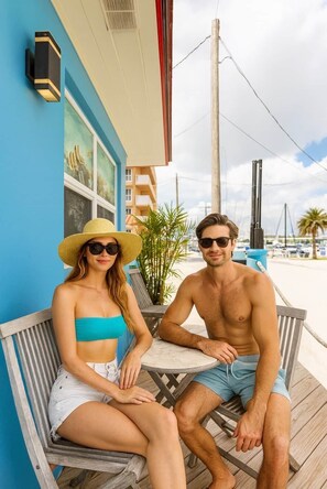 A couple seated on a wooden bench outside a building with a blue exterior. - The Emerald Palms Tropical Beach Villa (Hollywood)