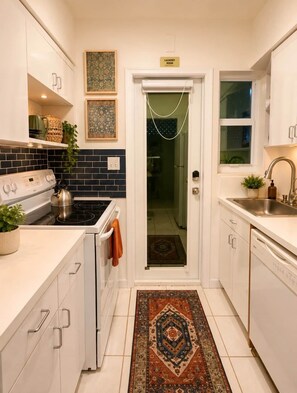 A compact kitchen with white cabinets, a stove, a sink, and a door leading to a laundry room. - The Emerald Palms Tropical Beach Villa (Hollywood)