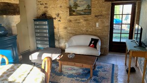 Una stanza rustica con un muro in pietra, un divano bianco, un tavolo di legno e una piccola credenza.