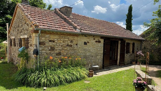 Una casa in pietra con tetto in tegole, una porta in legno e un piccolo giardino fiorito con erba.