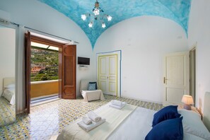 A bedroom with a bed, a chair, a TV, and a view of the outside. - Barbera House (Positano)