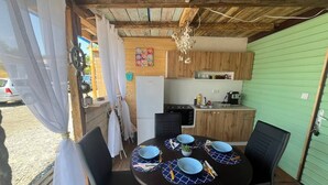 Un'area pranzo con un tavolo rotondo apparecchiato per quattro persone, circondato da sedie. Si intravede sullo sfondo una cucina con pensili in legno e un frigorifero.