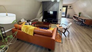 A modern living room with a brown leather sofa, a TV, and a dining area with a table and chairs.