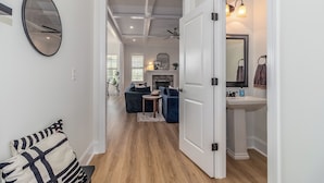 A hallway with a sofa, a round mirror, and a white door leading to a bathroom with a sink and a mirror. - Masters Week Stay in Bartram Trail Golf Community! (Evans)