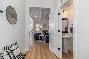 A hallway with a sofa, a round mirror, and a white door leading to a bathroom with a sink and a mirror. - Masters Week Stay in Bartram Trail Golf Community! (Evans)