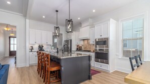 A modern kitchen with white cabinets, a central island with bar stools, stainless steel appliances, and pendant lighting. - Masters Week Stay in Bartram Trail Golf Community! (Evans)
