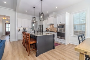 A modern kitchen with white cabinets, a central island with bar stools, stainless steel appliances, and pendant lighting. - Masters Week Stay in Bartram Trail Golf Community! (Evans)