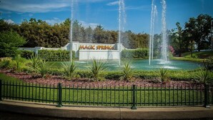 En springvand med flere stråler, omgivet af en velplejet have og et skilt, der står 'Magic Springs'.