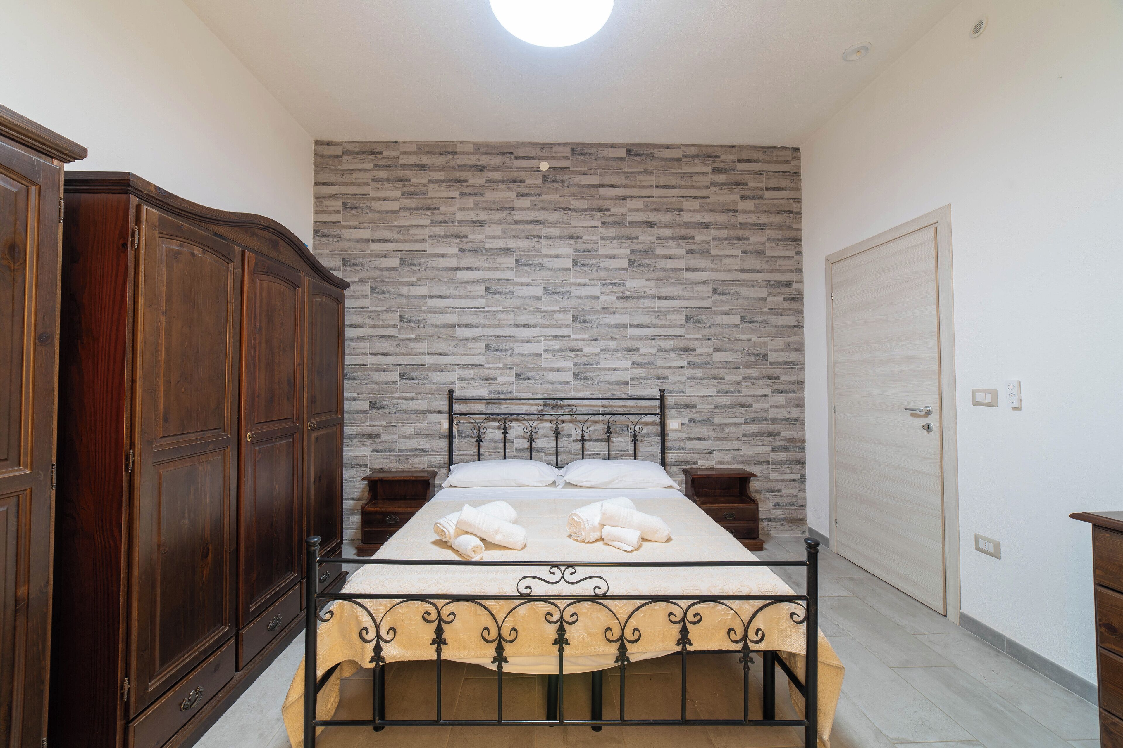 A bedroom with a bed, wooden wardrobe, and a stone-patterned wall.