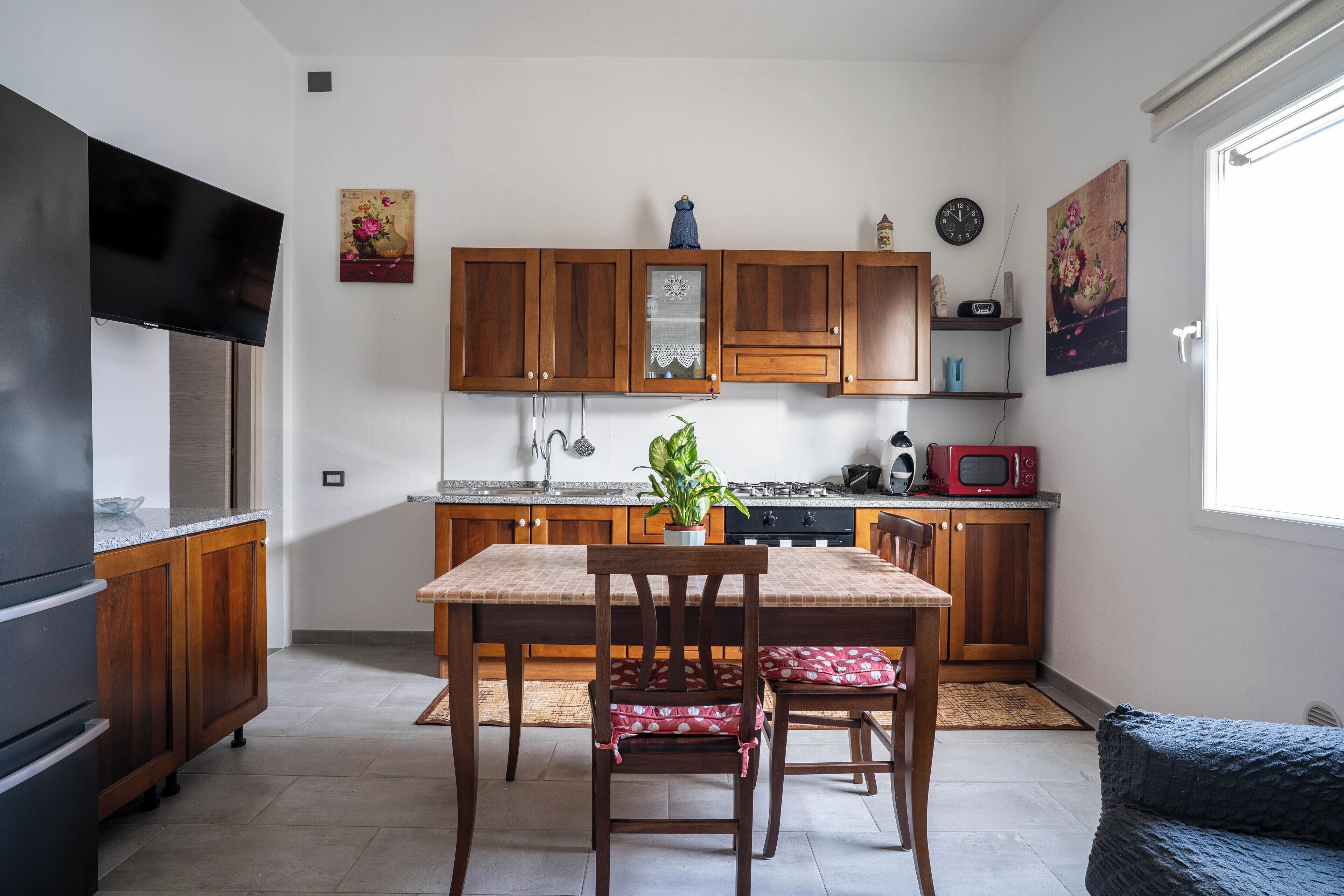 A compact kitchen with wooden cabinets, a dining table with chairs, a TV, and a microwave.