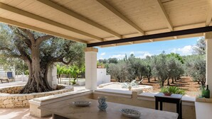 An outdoor patio with a stone table, a large tree, and a view of an olive grove. - Trullo Solleone by Perle di Puglia (Carovigno)