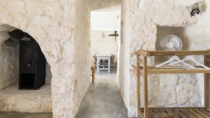 A narrow stone corridor with a fireplace, a wooden table with chairs, and a fan on a wooden stand. - Trullo Solleone by Perle di Puglia (Carovigno)