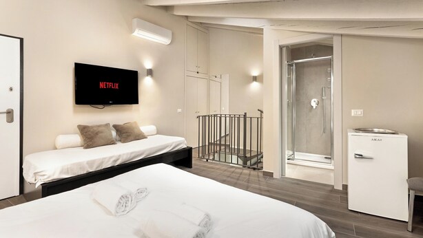 Habitación de hotel moderna con cama, televisor montado en la pared, refrigerador pequeño y zona de ducha.