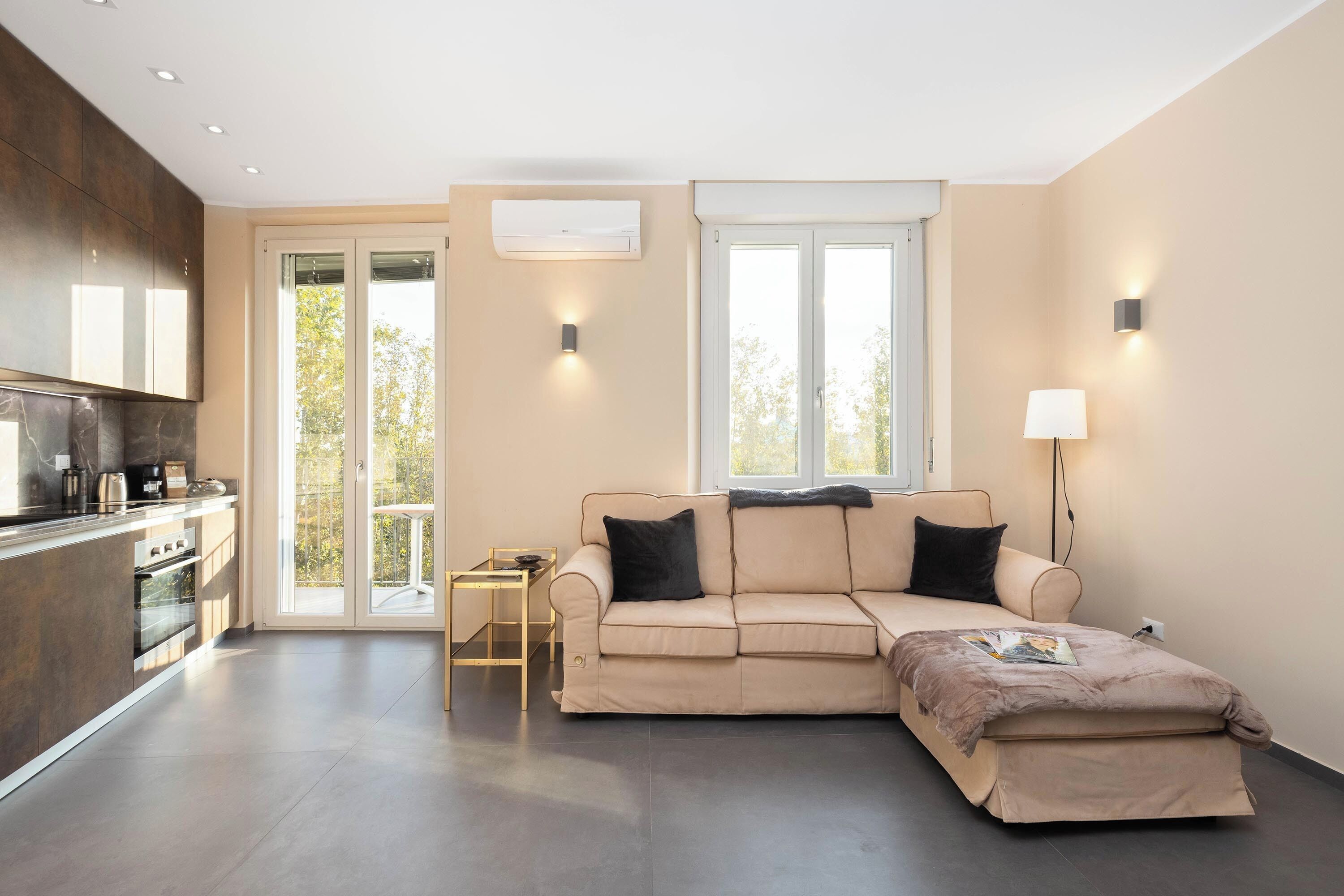 A modern living room with a sofa, a coffee table, and a TV. There is a sliding glass door leading to a balcony.