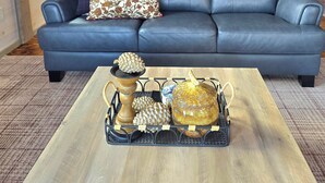 Una sala de estar moderna con un sofá de cuero azul, una mesa de centro de madera con objetos decorativos y un cuadro de árboles en la pared.