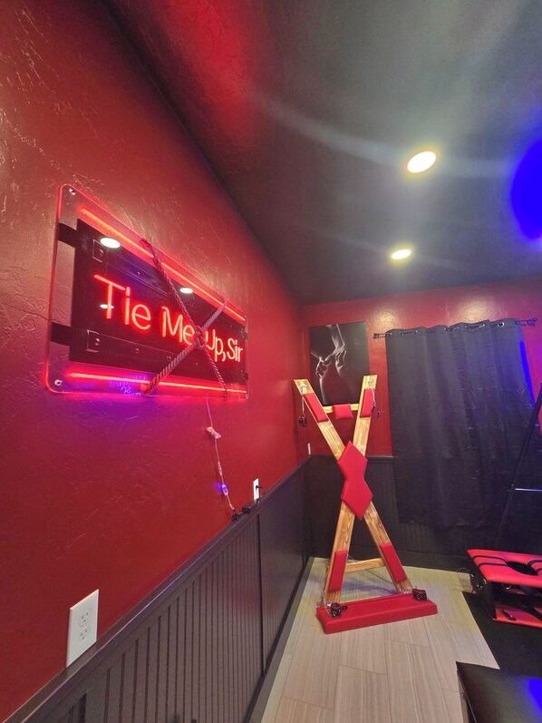 Pared roja con un letrero de neón que dice 'Tie Me Up Sir'.