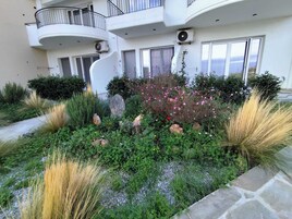 A multi-story building with balconies, a garden with various plants and flowers, and a stone pathway.