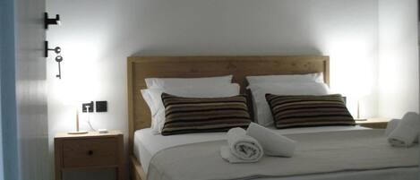 A neatly made bed with striped pillows, a wooden headboard, a nightstand with a lamp, and a wall-mounted key holder.